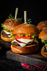Several homemade burgers with cheese on a black background, vertical photo