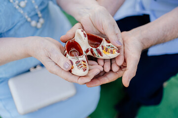 hands of elderly couple hold ceramic casket shoe with wedding rings. Anniversary