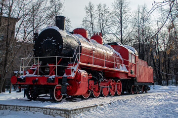 A red steam locomotive stands on a platform covered in snow.