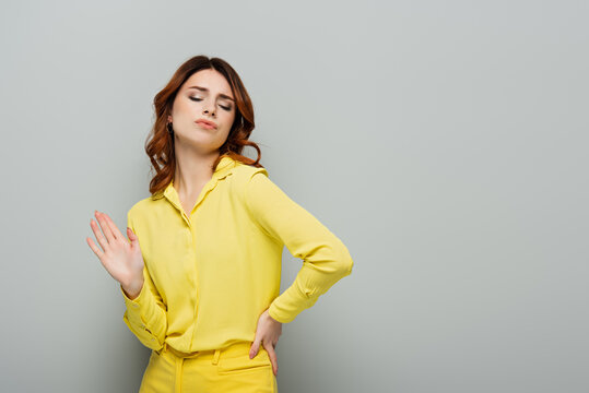 smug woman showing refuse gesture while standing with hand on hip on grey