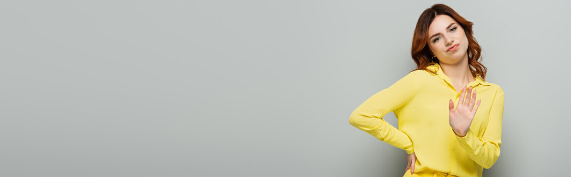 skeptical woman showing refuse gesture while standing with hand on hip on grey, banner