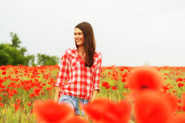 Young beautiful woman walking at poppy field. Happy girl among blooming red flowers, spring nature outdoor