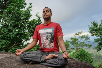 man meditating at rock in deep green forests for spiritual enlightenment