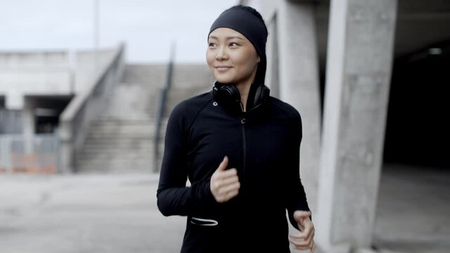 Asian woman jogging in urban environment, looking around and smiling. Urban city lifestyle. Active woman runner exercising outside. 