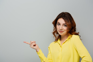 smirking woman looking at camera while pointing with finger on grey