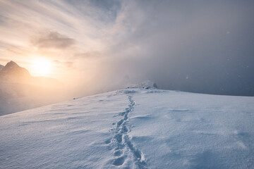 Fototapeta na wymiar Sunrise on snowy mountain with footprint in blizzard at Senja Island