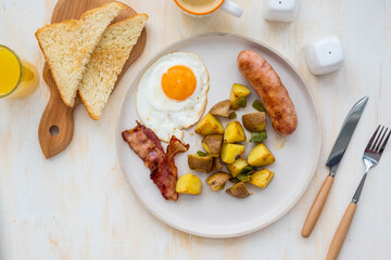 Traditional American full breakfast with scrambled eggs, fried potatoes, pork sausage and bacon on a white ceramic plate on a light concrete background. American cuisine.