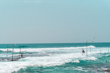 Tropikalna plaża z palmami, niebieski ocean z falami oraz kije rybackie.