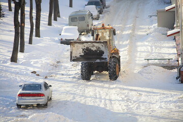 A big bulldozer tractor removes a snow with scraper shovel blade snowplow on courtyard road near...