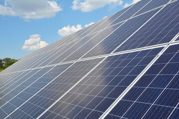 A close-up on a solar panel with numerous solar modules and photovoltaic cells against blue sky with white clouds as a source of alternative, renewable green energy.