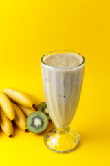 Banana and kiwi milkshake in glass with kiwi and bananas on yellow background