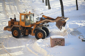 One yellow heavy wheeled tractor removes a snow with scraper shovel blade snowplow in the Park near...