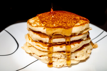 Syrup pouring onto a stack of fluffy pancakes against a black background.