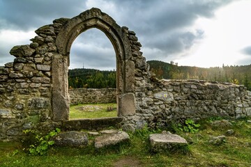 Fototapeta na wymiar Tridomi, Czech Republic - October 29 2016: Stone ruins of the former medieval church of St Nicholas, svaty Mikulas, standing in the middle of the forest. View of the door. Sun over horizon.