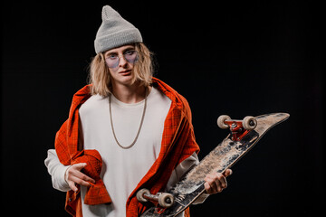 Portrait of a stylish man holding a skateboard in the Studio. Close-up of a smiling skateboarder posing on a black background