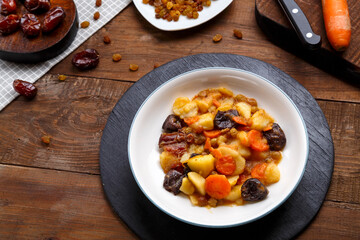 A dish of Jewish cuisine sweet tsimes with vegetarian dates carrots in a plate on a round stand next to candied fruits.