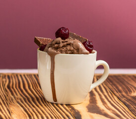 pudding with ice cream, cherries and pieces of chocolate in a mug on a jjon wood table. Melted ice cream flows in a mug on a pink background. High quality photo