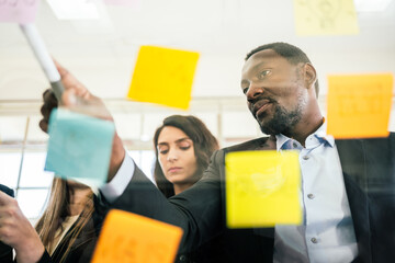 Close-up of smiling African businessman brainstorm meeting with colleagues by using colorful sticky paper note on glass wall for finding new ideas. Using agile methodology and do business.