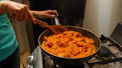 closeup hands of young latin woman cooking chicken and spices in barbecue sauce at home