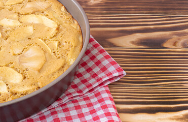 homemade apple pie just from the oven in a baking dish. Stands on a red-white checkered napkin on a burnt wooden background. Homemade baking concept, simple recipe. High quality photo