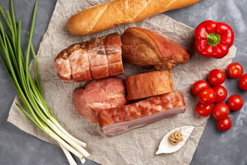Variety of smoked pork with cherry tomatoes on parchment. View from above. Assorted semi-finished meat products.