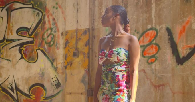 A young woman stands next to grafitti on a wall in an abandoned warehouse