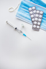 Preparation for vaccination against covid-19. Syringe, vaccine, pills, medical mask on a white table. View from above.