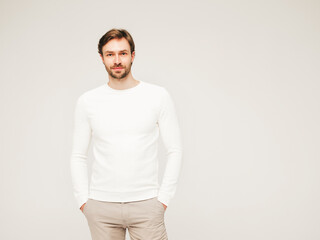 Portrait of handsome smiling hipster lumbersexual businessman model wearing casual white sweater and trousers. Fashion stylish man posing against gray background in studio