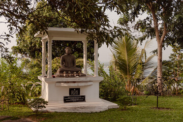 Posąg Buddy na tle zieleni w buddyjskiej świątyni. - obrazy, fototapety, plakaty