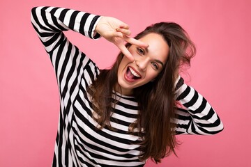 Fototapeta premium Photo of young european positive smiling winsome happy beautiful brunette female person with sincere emotions wearing casual striped pullover isolated on pink background with copy space