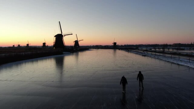 On an early morning in February the sunrise in Kinderdijk, Unesco heritage site with iceskating persons, filmed with a drone.  6 windmills in the picture.