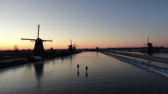 On an early morning in February the sunrise in Kinderdijk, Unesco heritage site with iceskating persons, filmed with a drone.  9 windmills in the picture.