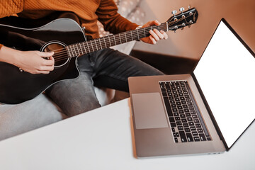 Man learning to play guitar with the help of online learning at home. Guy sitting at table with...