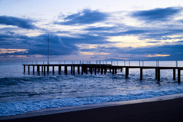 View from beach to water of sea, waves with white foam, pierce and sky with clouds in a nice evening.