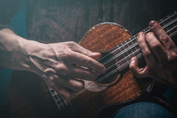 Hands of a man playing the ukulele. Folk music performer on ukulele. Photo with toning and shallow...