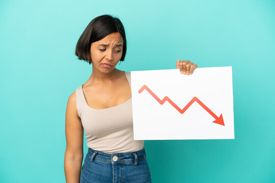 Young mixed race woman isolated on blue background holding a sign with a decreasing statistics arrow symbol with sad expression