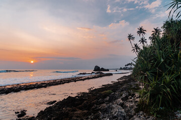 Pomarańczowo fioletowe niebo z zachodzącym słońcem, tropikalny krajobraz wybrzeże z oceanem. © insomniafoto