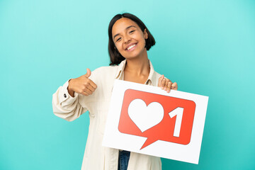 Young mixed race woman isolated on blue background holding a placard with Like icon with thumb up