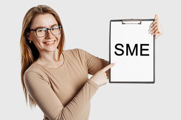 sme. Beautiful young business woman wearing glasses holds a clipboard with mock up space isolated on gray background