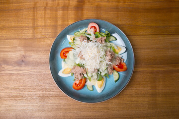 Top view photo of fresh salad with eggs, ton, salad and parmesan on wooden table.