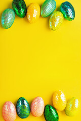 Frame made from multicolored glossy easter eggs.Trendy yellow background.Creative layout with copy space.Vertical photography.