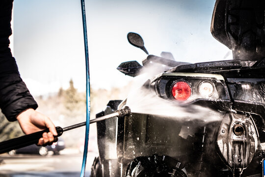 A Young Man Is Washing His Dirty ATV On The Car Wash.
