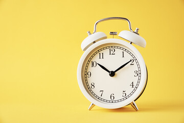 White vintage alarm clock on a yellow background with copy space