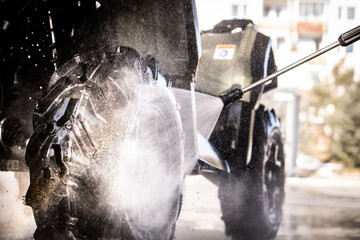 A young man is washing his dirty ATV on the car wash.