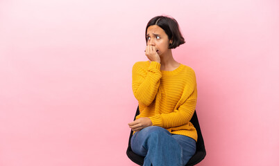Young mixed race woman sitting on a chair isolated on pink background nervous and scared