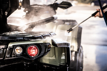 A young man is washing his dirty ATV on the car wash. © Nataly