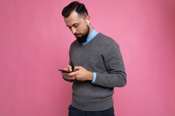side-profile Photo shot of handsome positive good looking young man wearing casual stylish outfit poising isolated on background with empty space holding in hand and using mobile phone messaging sms