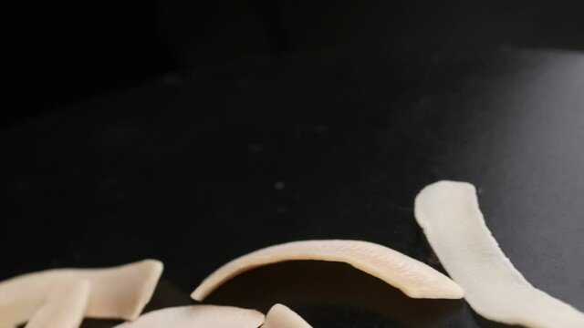 Coconut chips on a dark table close-up. Black background, slow motion.