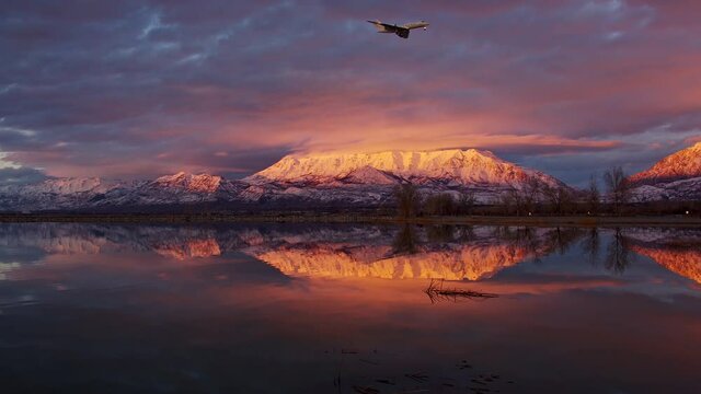 Airplane flying through the sky during colorful sunset with snow capped mountain reflecting in Utah lake as the plane is about to land at the Provo Airport.