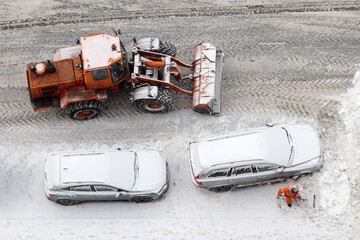 Worker and snow plow machine removing the snow on the parking lot, top view. Snowfall in winter...